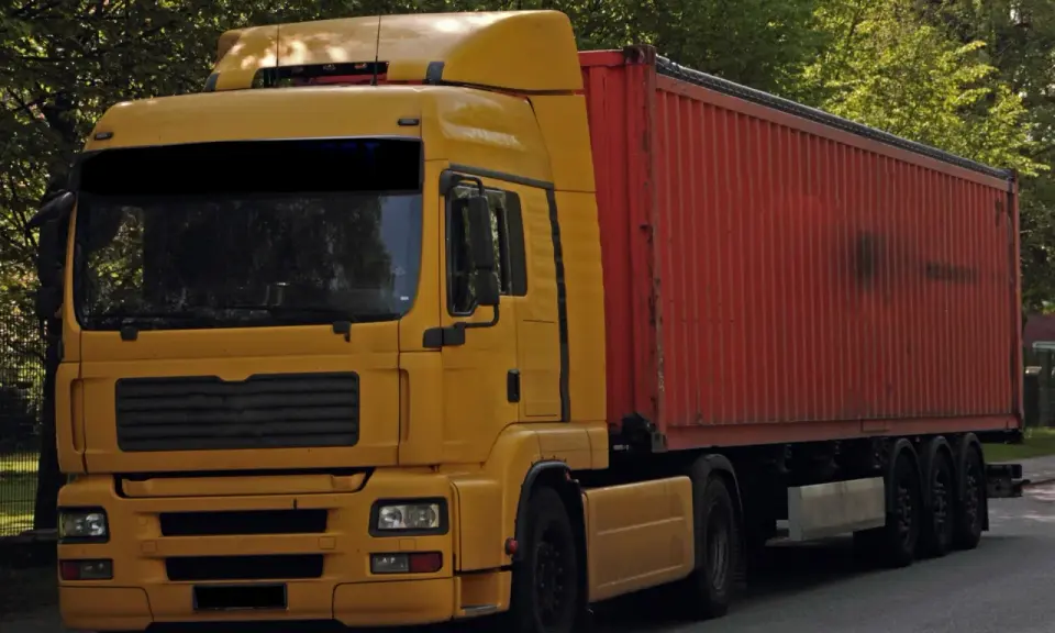 Żółta ciężarówka z czerwonym kontenerem, to pojazd drogowy bez silnika, gotowy do transportu.