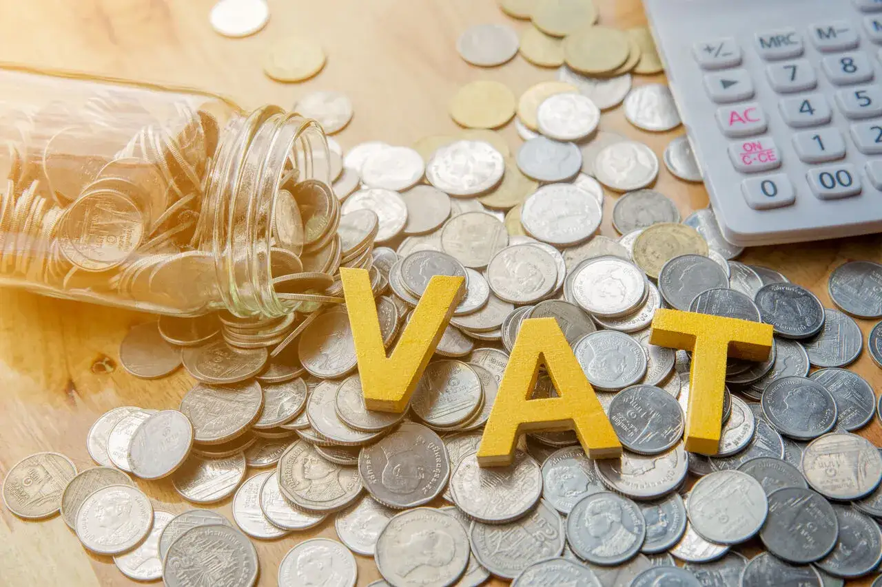 Skarbonka z monetami, litery VAT i kalkulator. Przygotowania do limit vat 2026.