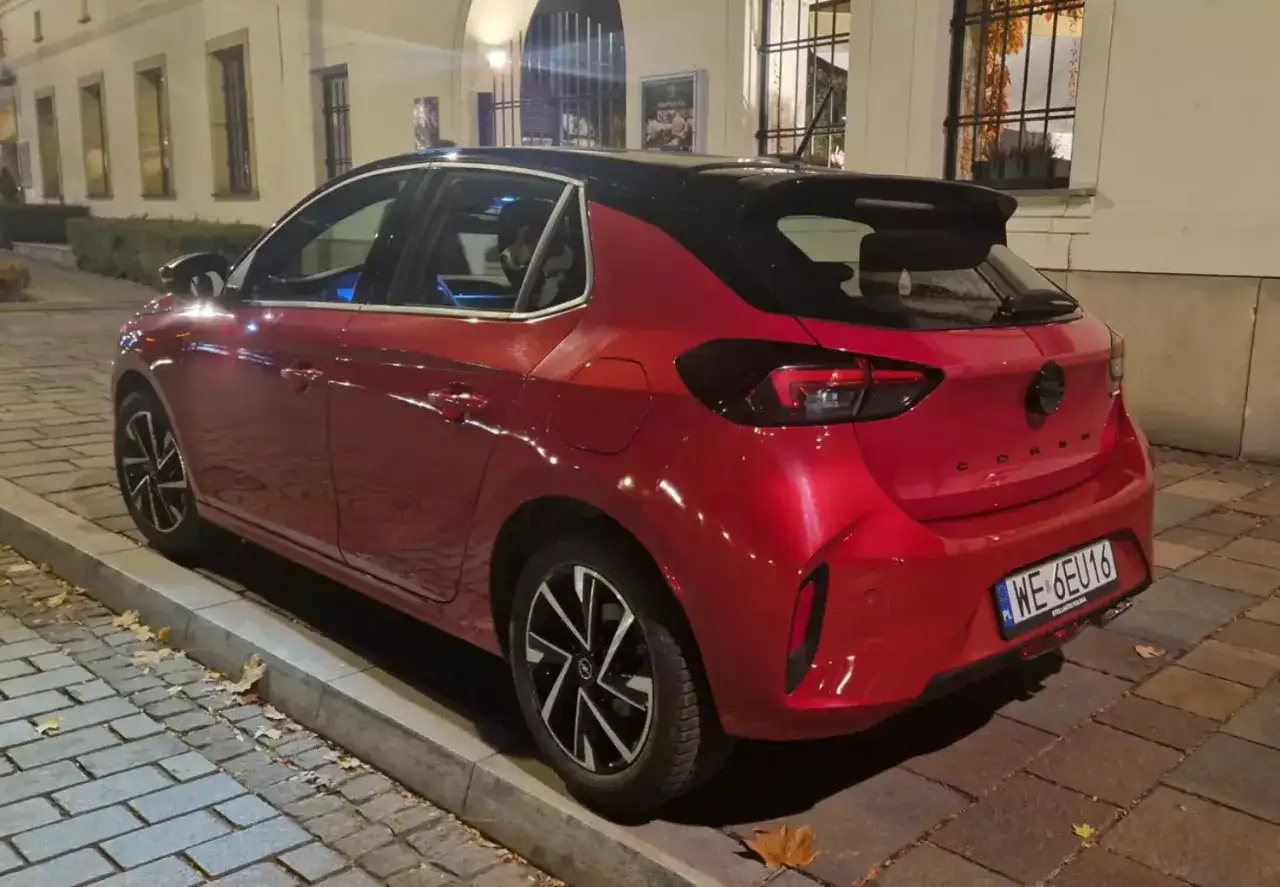 Czerwony samochód firmowy Opel Corsa zaparkowany na ulicy. Po zawieszeniu działalności, auto czeka na nowego właściciela.