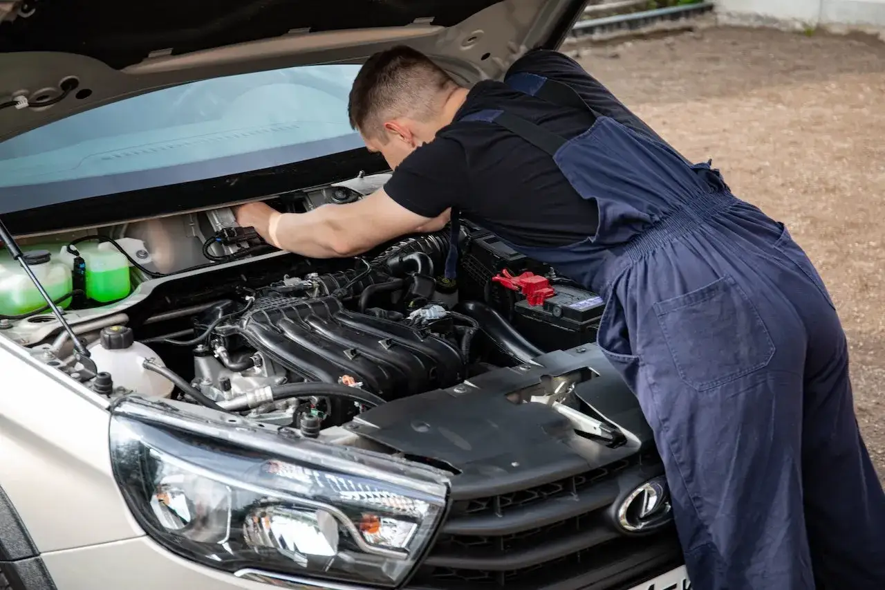 Mechanik w niebieskim kombinezonie pracuje przy silniku samochodu, pokazując, jak stosować płukankę do silnika.