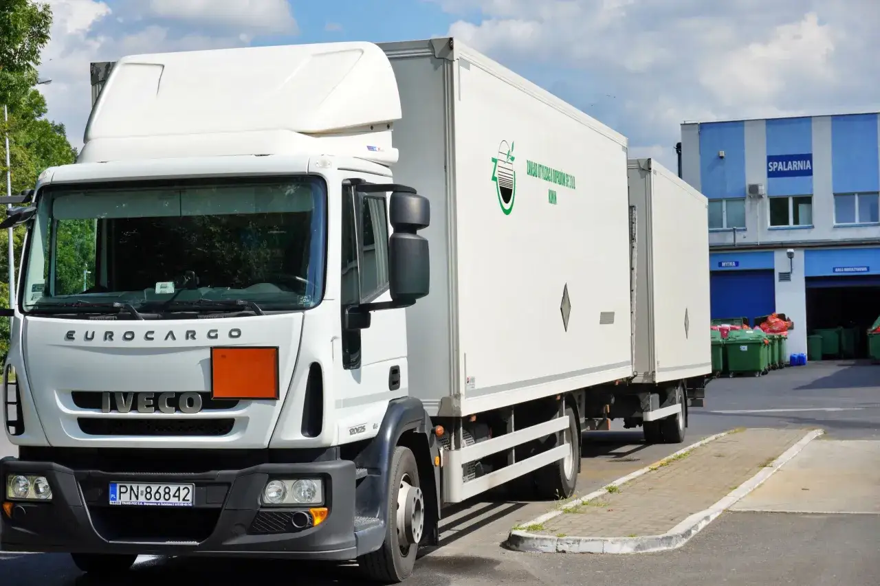 Biała ciężarówka Iveco z naczepą, gotowa do transportu odpadów niebezpiecznych. Na naczepie logo firmy