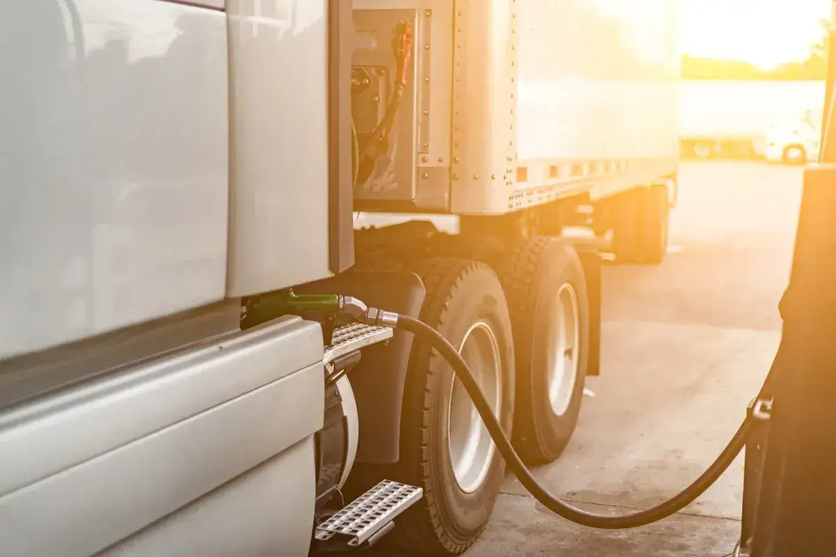Ciężarówka tankuje paliwo, co wpływa na koszty w transporcie. Widoczne koła i wąż paliwowy.