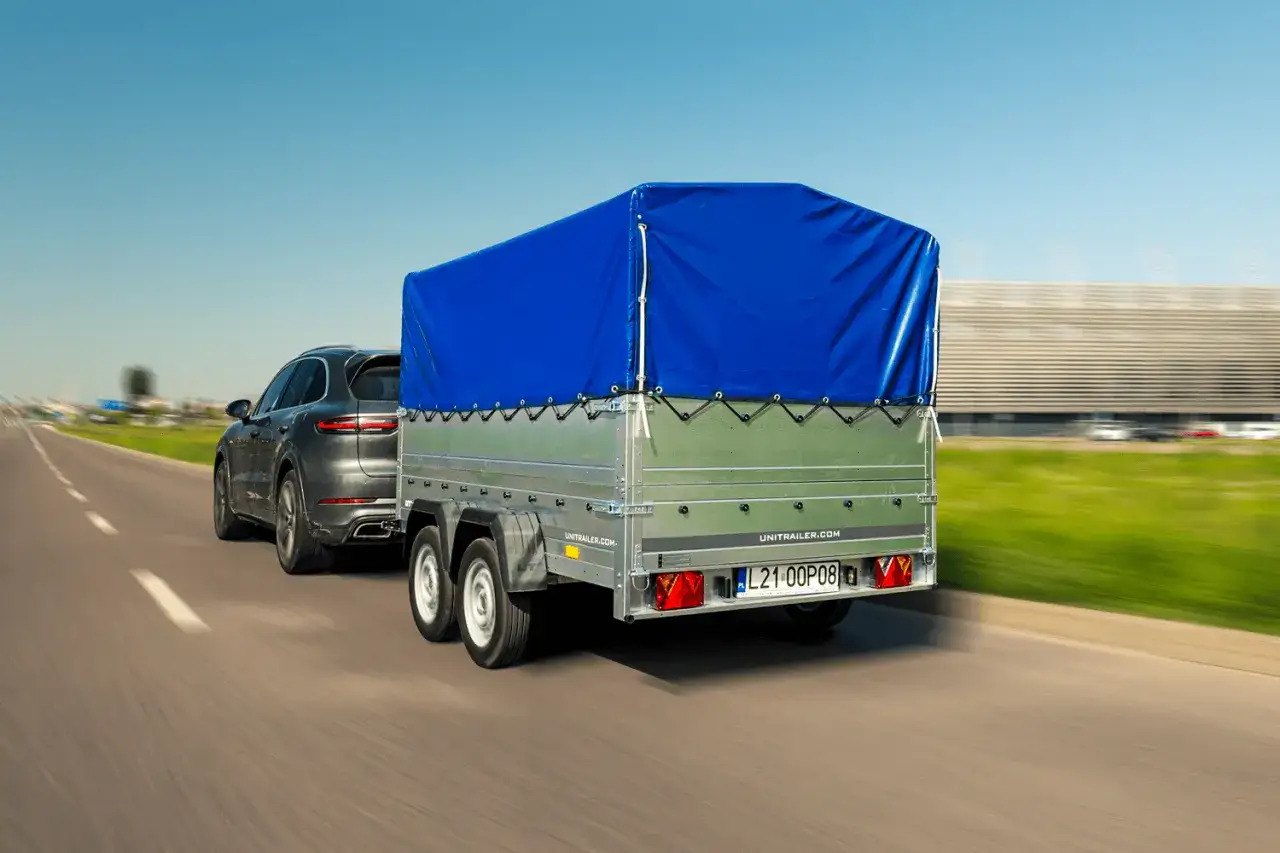Ciemnoszary SUV ciągnie przyczepę z niebieską plandeką. Czy przyczepa to pojazd? Tak, gdy jest holowana przez samoch&oacute;d.