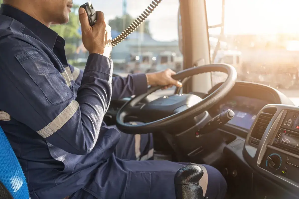 Kierowca w mundurze używa krótkofalówki, prowadząc ciężarówkę. To symbol odpowiedzialności spedytora za bezpieczny transport.