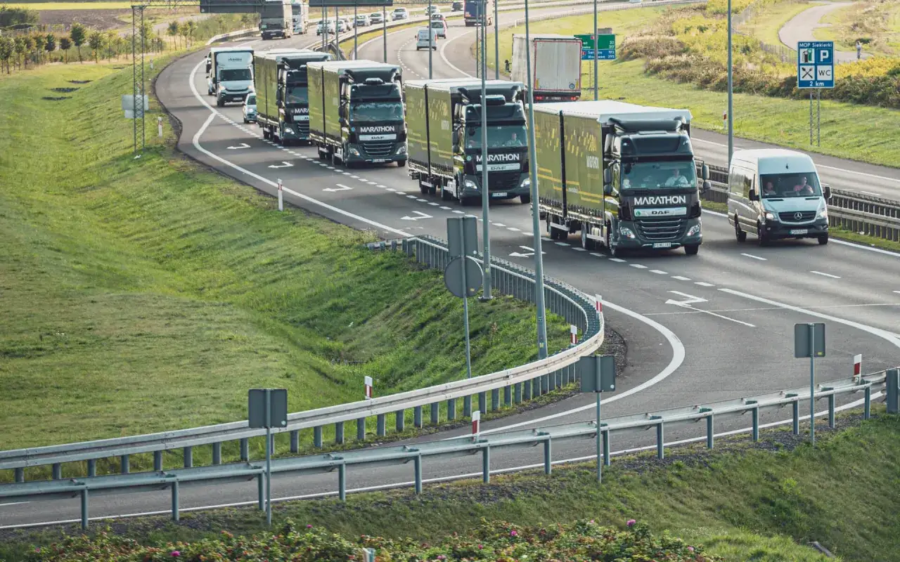 Konwój ciężarówek, czyli tirów, jedzie autostradą. Widać też mniejszego vana.