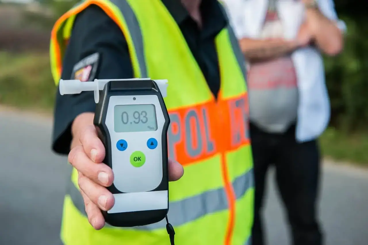 Policjant pokazuje alkomat z wynikiem 0.93 promila. Przypomnienie o zagrożeniach związanych z pijani kierowcy statystyki.