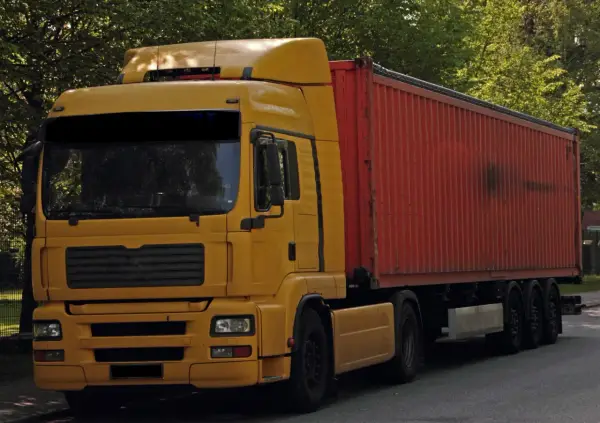 Żółta ciężarówka z czerwonym kontenerem, to pojazd drogowy bez silnika, gotowy do transportu.