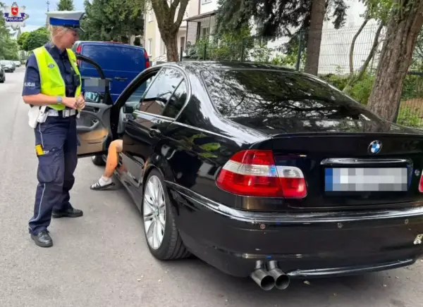 Policjantka zatrzymała kierowcę czarnego BMW. Kierowca wysiada z auta, prawdopodobnie czeka go więzienie za przekroczenie prędkości.
